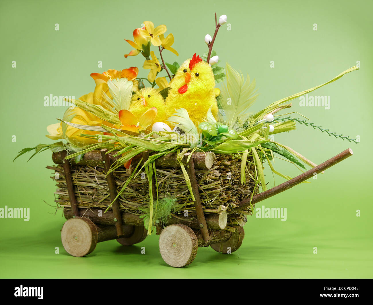 Wicker cart with Easter chickling and eggs over light green background Stock Photo