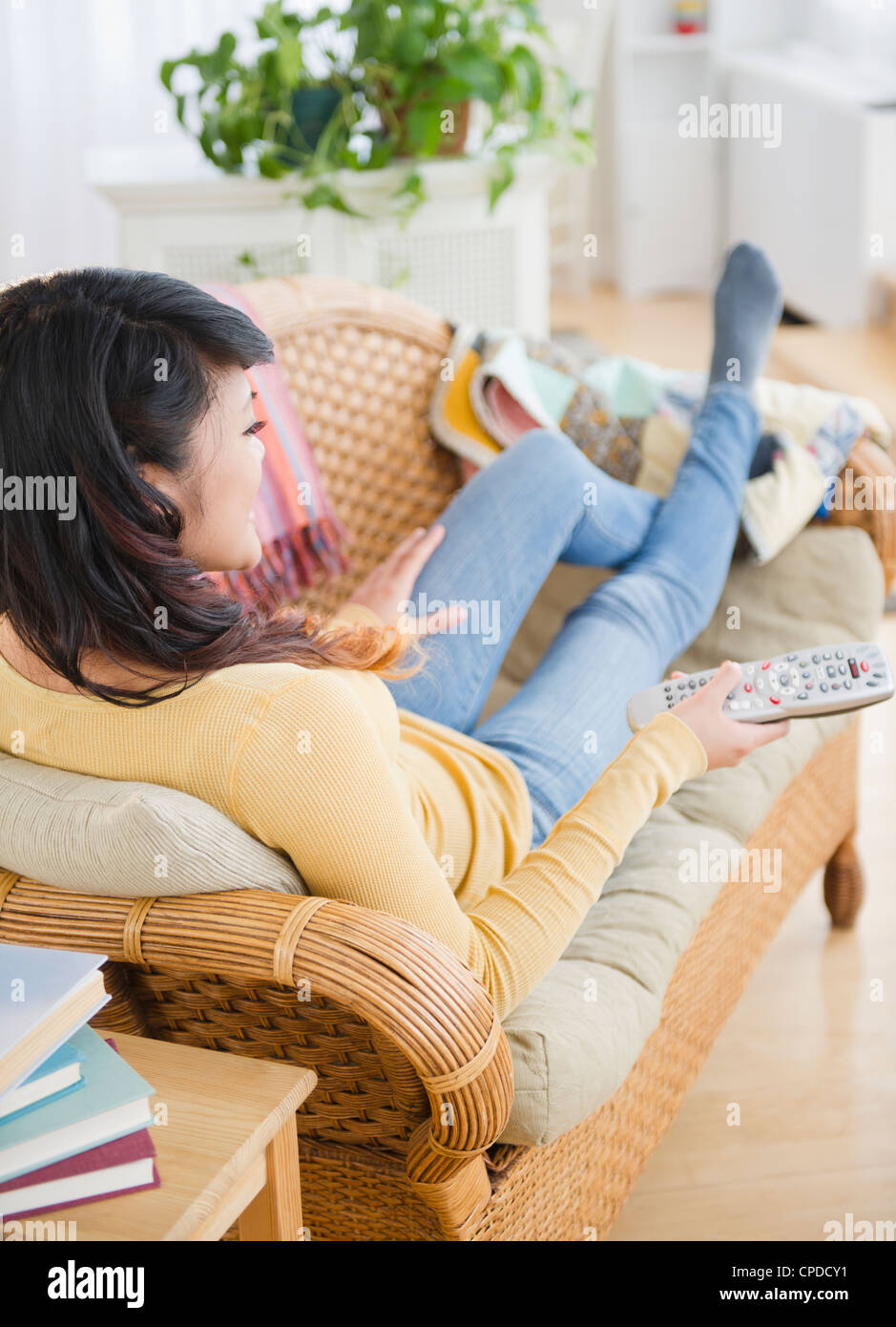 Pacific Islander woman laying on sofa watching television Stock Photo