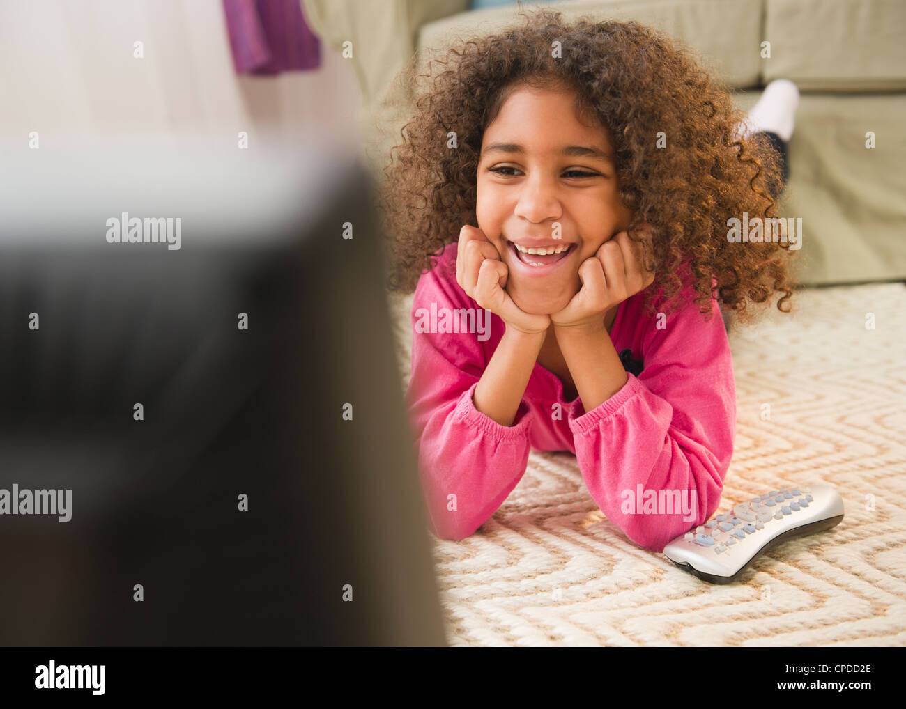 Mixed race girl laying on floor watching television Stock Photo