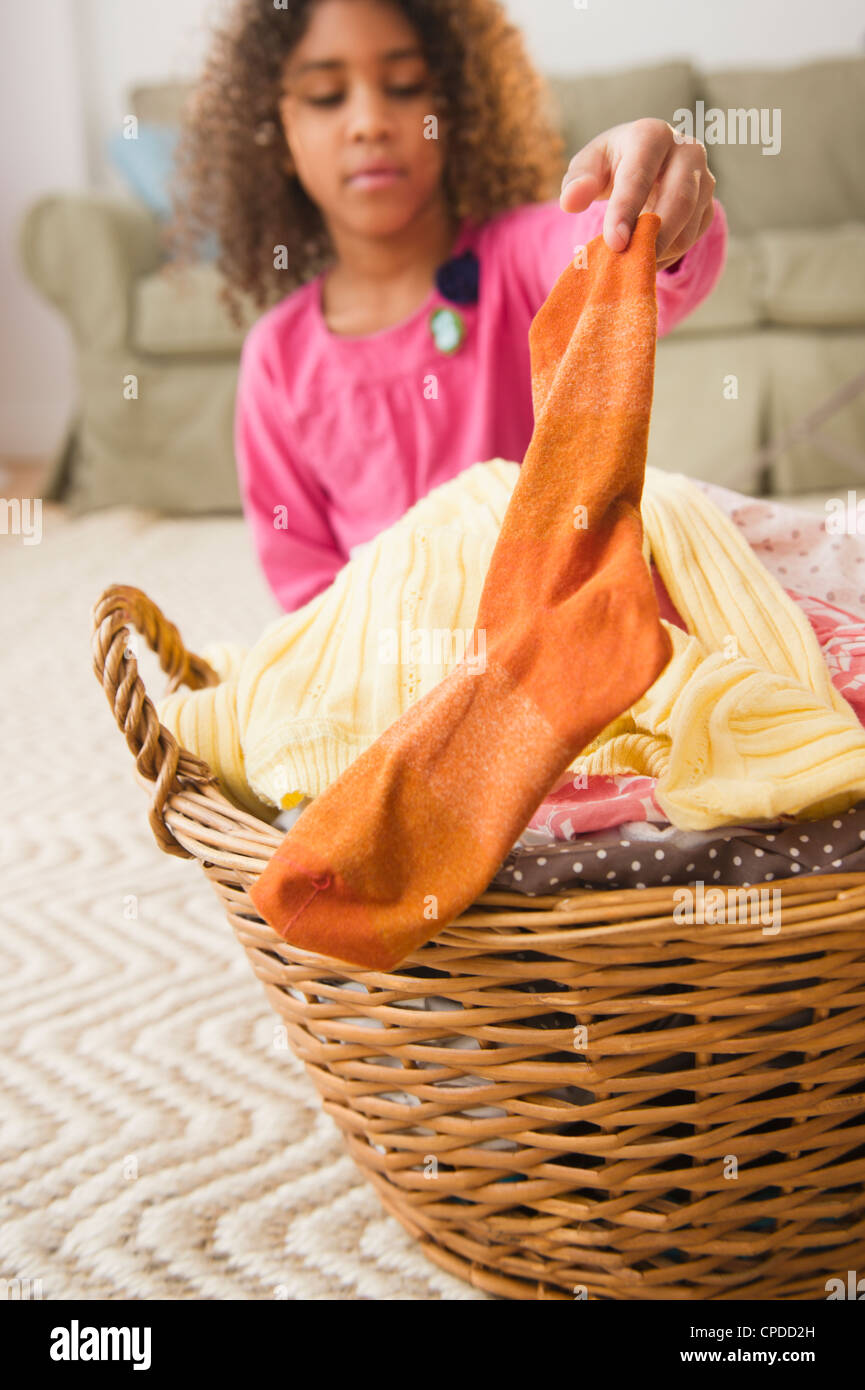 Mixed race girl putting sock into laundry basket Stock Photo Alamy