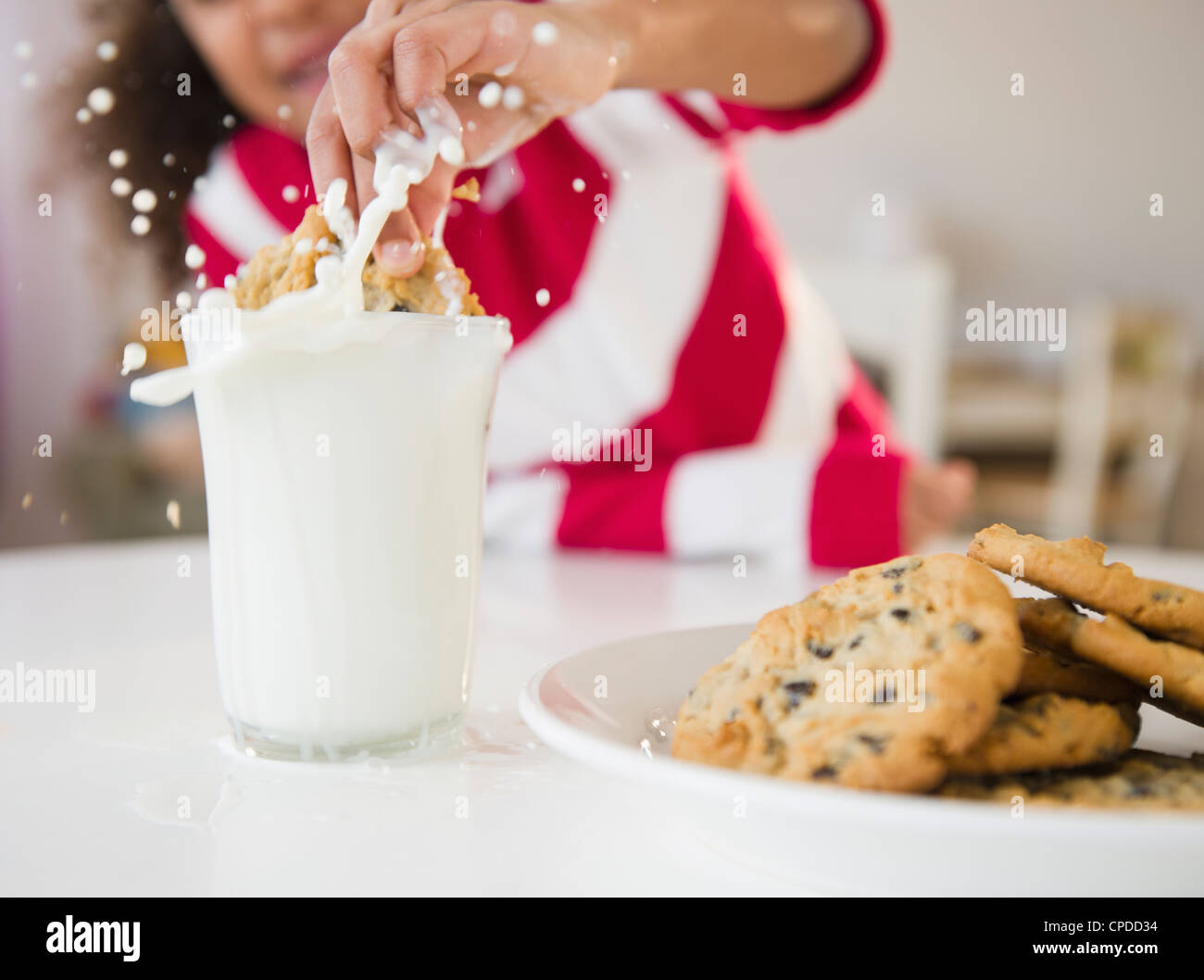 Mixed race girl dunking cookie into milk Stock Photo