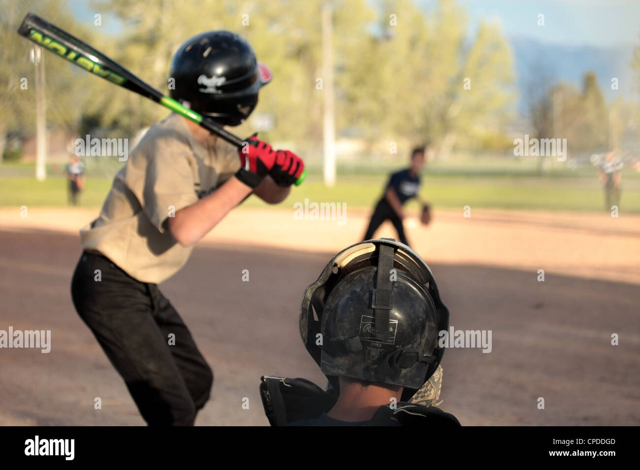 Little league baseball team players boy hits ball and runs to first base. Two teams in uniform. Small farming rural community. Stock Photo