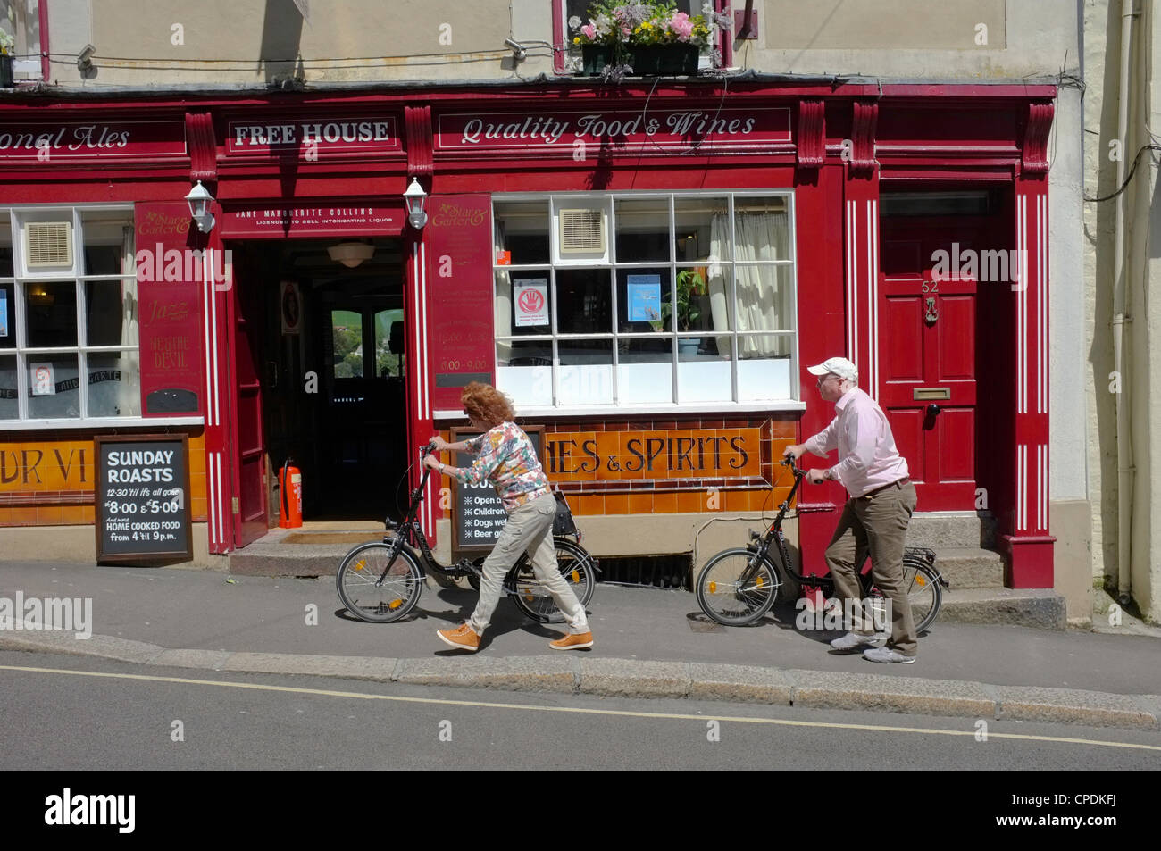 Two people push bikes past a pub in Falmouth, Cornwall Stock Photo