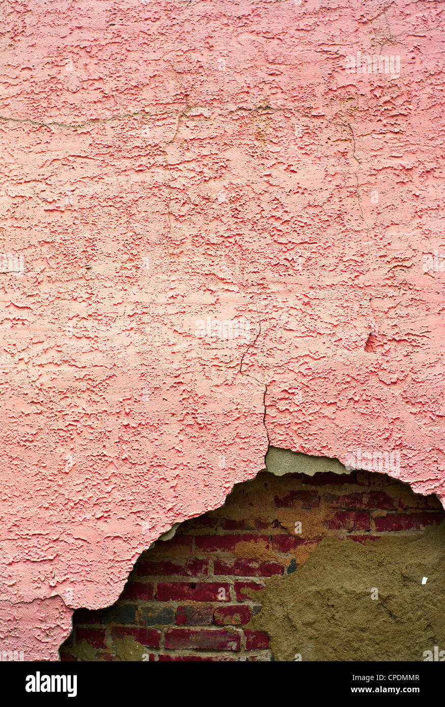 Cracked pink stucco wall revealing red brick wall behind it Stock Photo