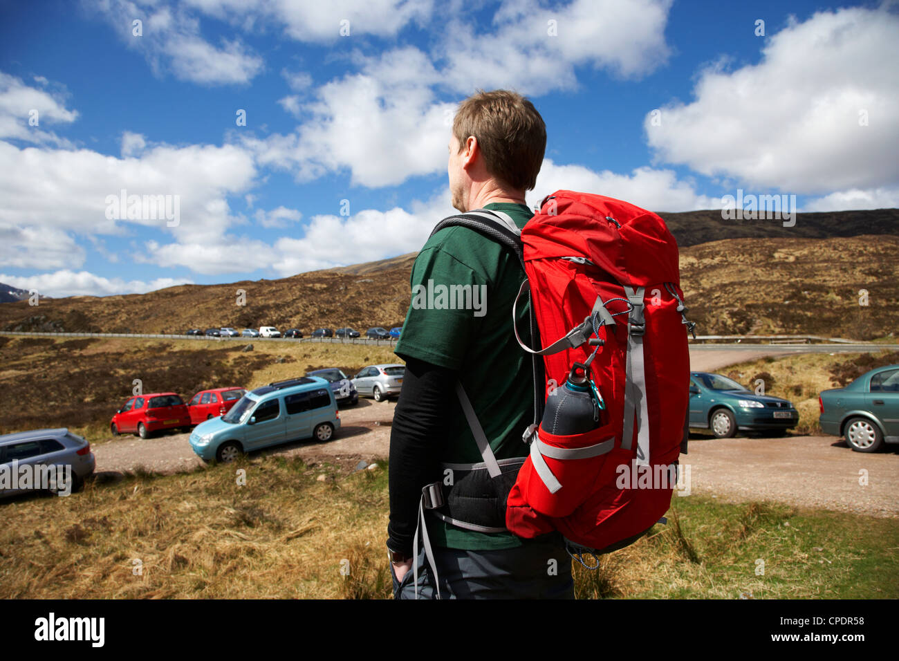 hiker hillwalker leaving busy side road with lots of cars parked in the
