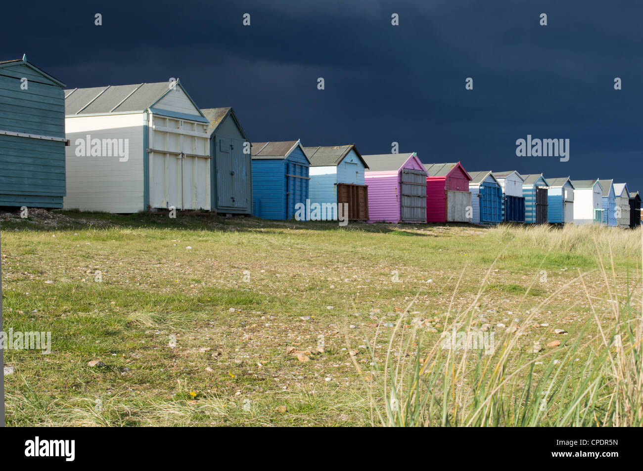 Beach huts in the sun with a dark, moody sky Stock Photo