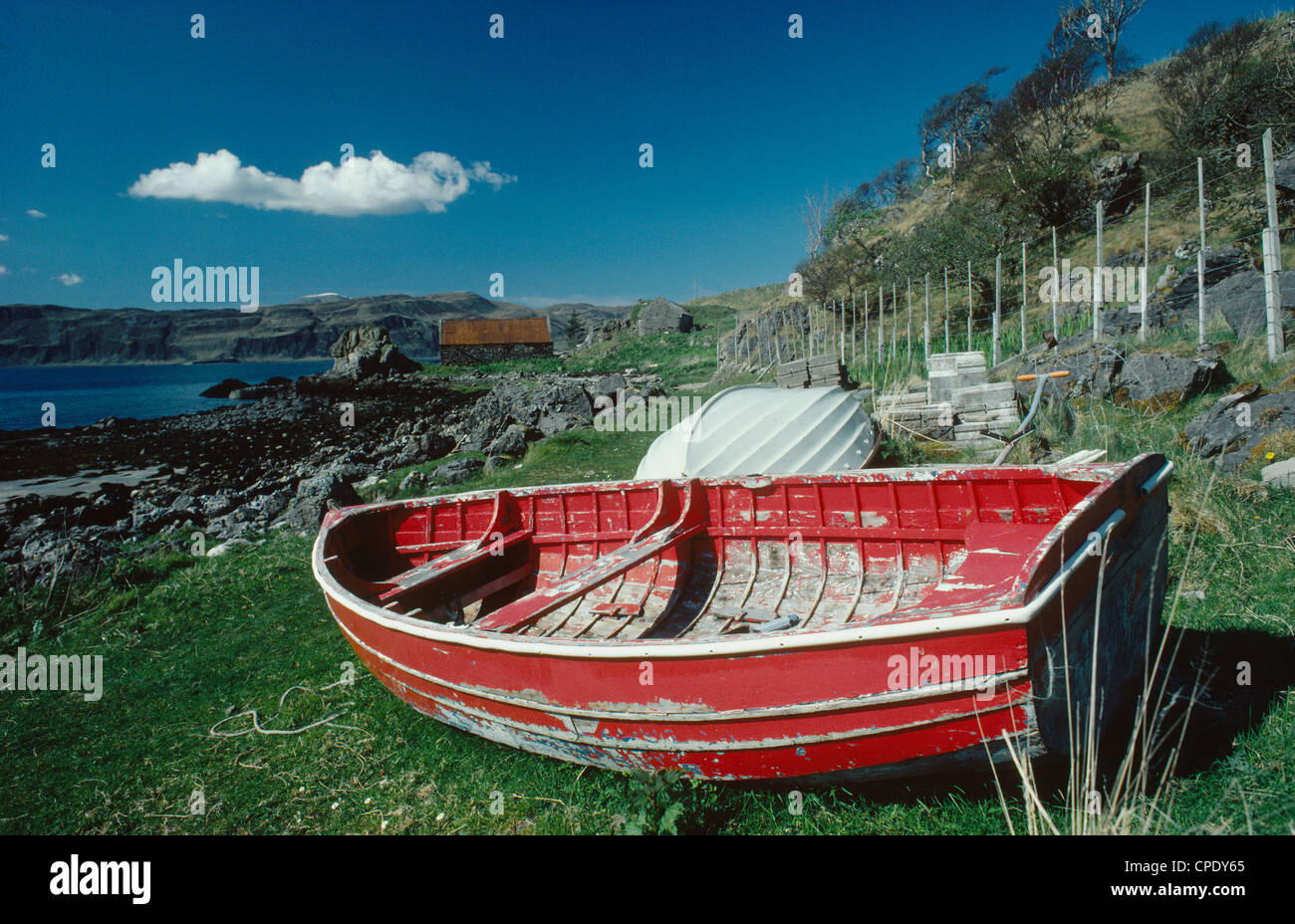 Beached red rowing-boat and solitary white cloud in a blue sky, at Ord, Sleat, southern Skye, western Scotland, UK Stock Photo
