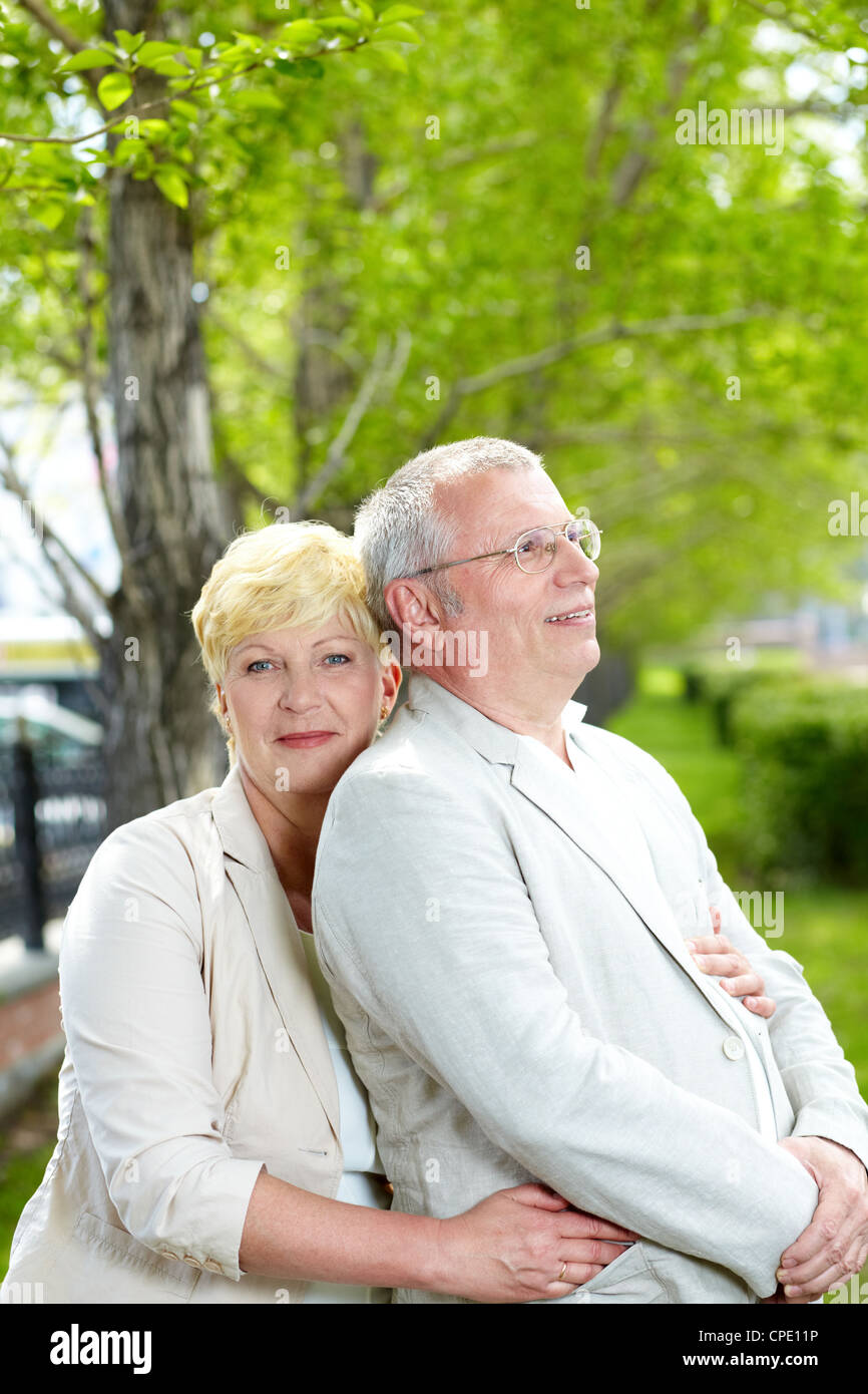 Mature woman looking at camera while embracing her husband outside Stock Photo