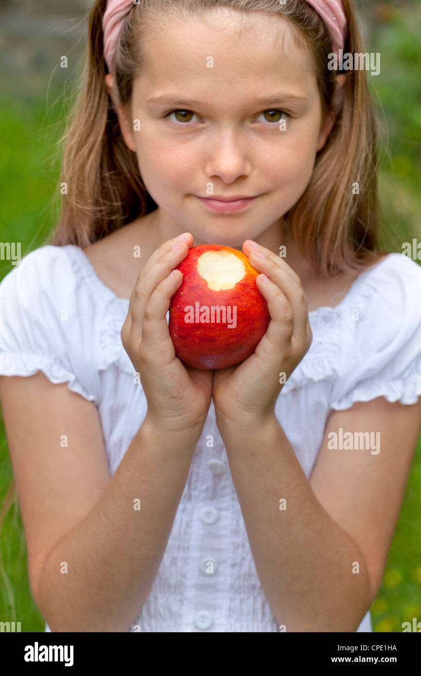 Girl standing outside in a field and shows a half-eaten apple Stock Photo