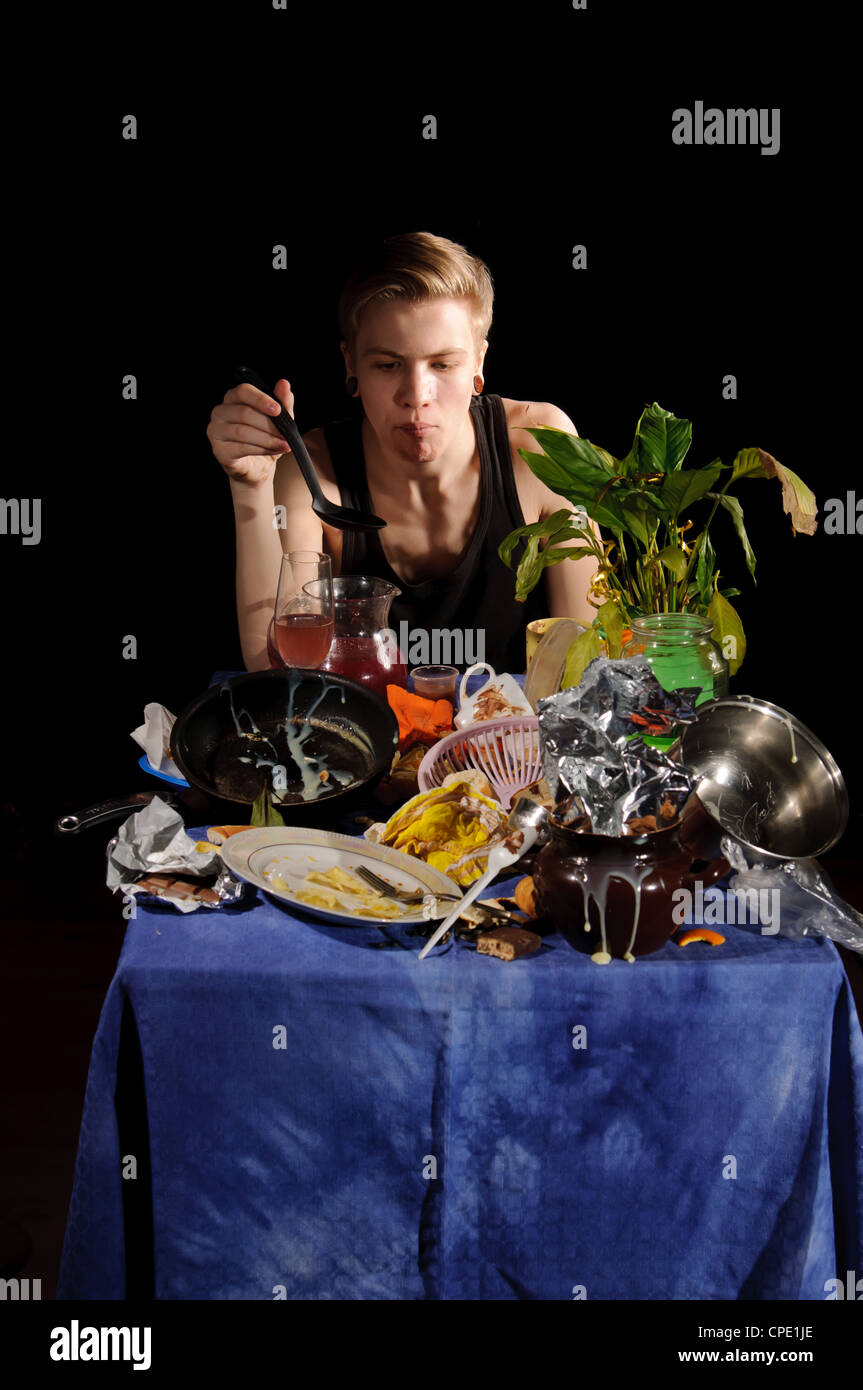 A young man with a spoon sits behind dirty table Stock Photo