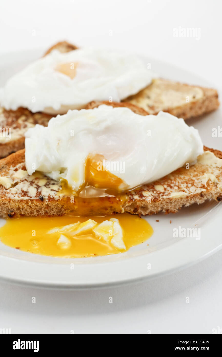 Close up of poached eggs with a soft golden yolk dripping onto the plate Stock Photo