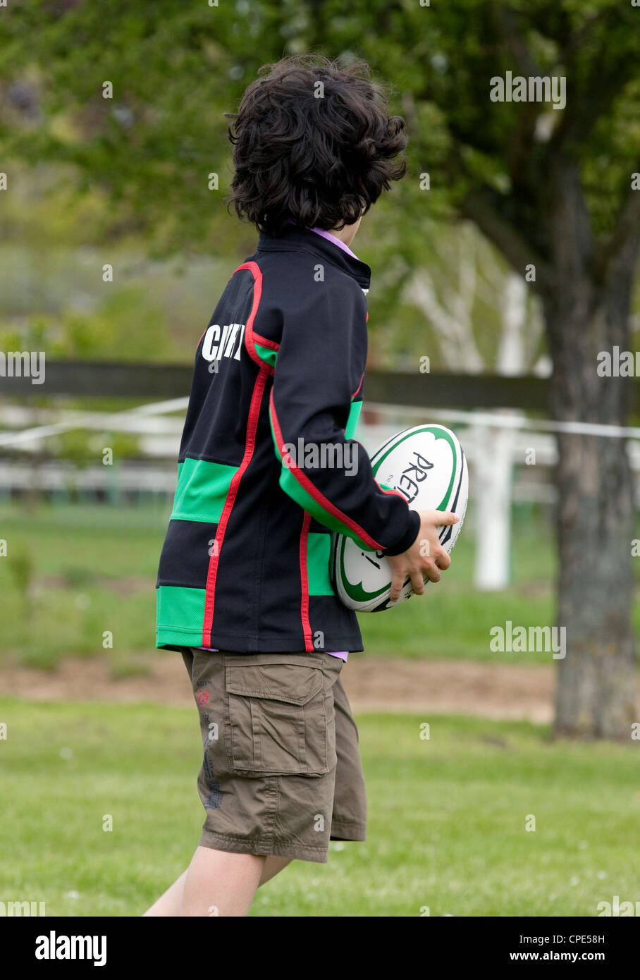 Young boy playing rugby, holding rugby ball, looking away, UK Stock
