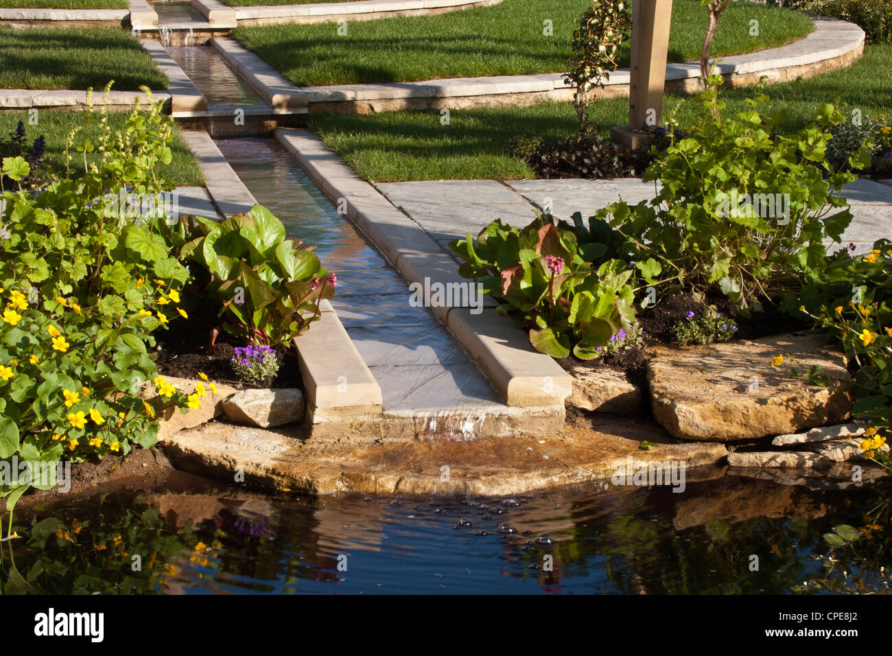 a garden with garden rill water feature made from stone and paved paving borders lawn lawns water marginal plants planting UK Stock Photo