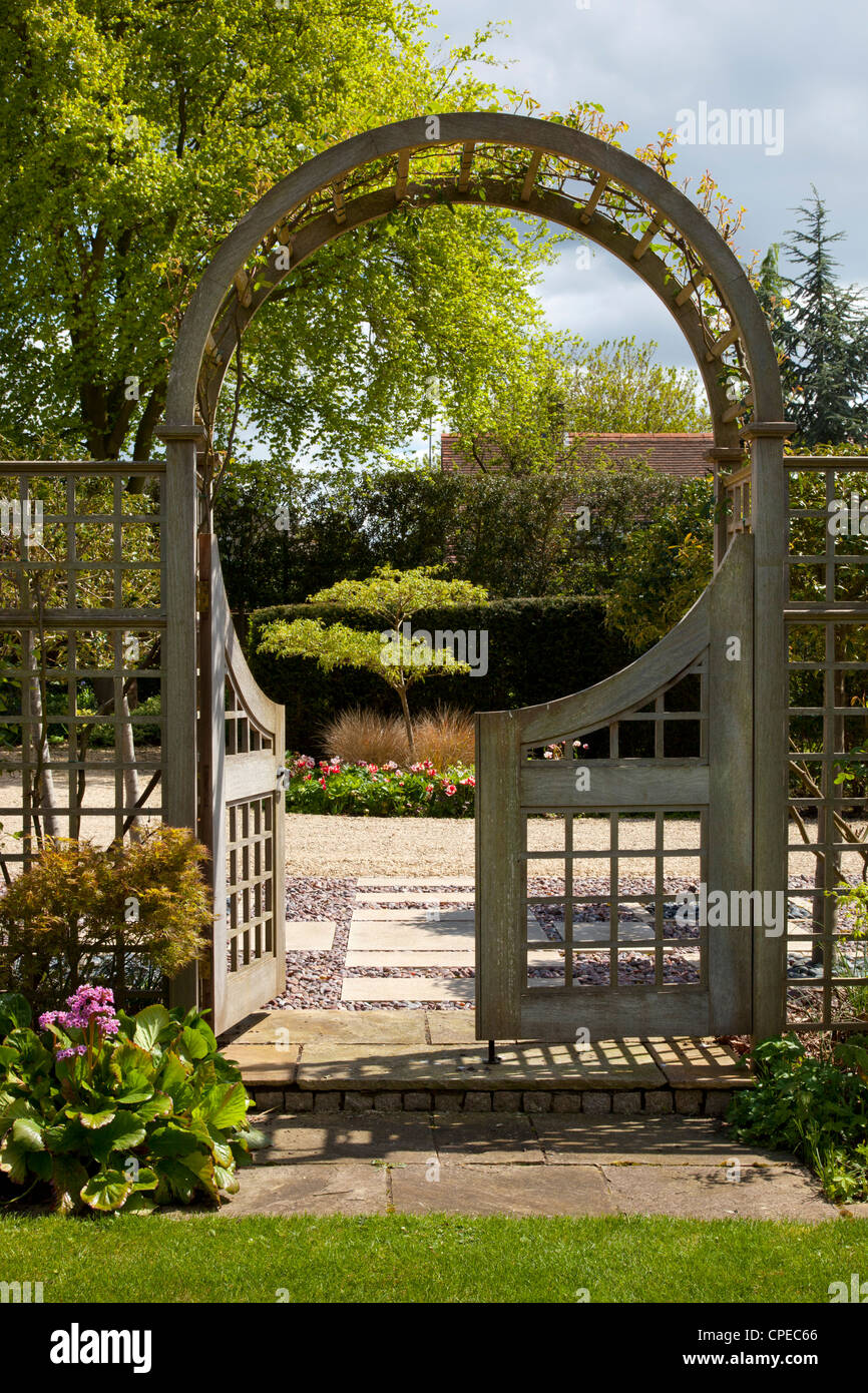 Garden feature Arch with gates leading into stone and pebble area with acer tree and tulips. Stock Photo
