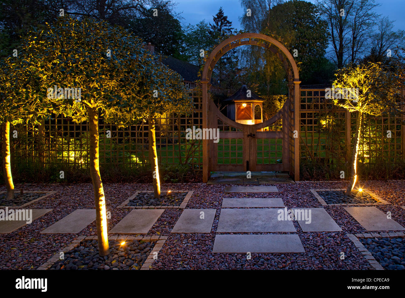 Garden feature Arch at night with holly trees lit and gates leading into lawn area with illuminated Gazebo Stock Photo