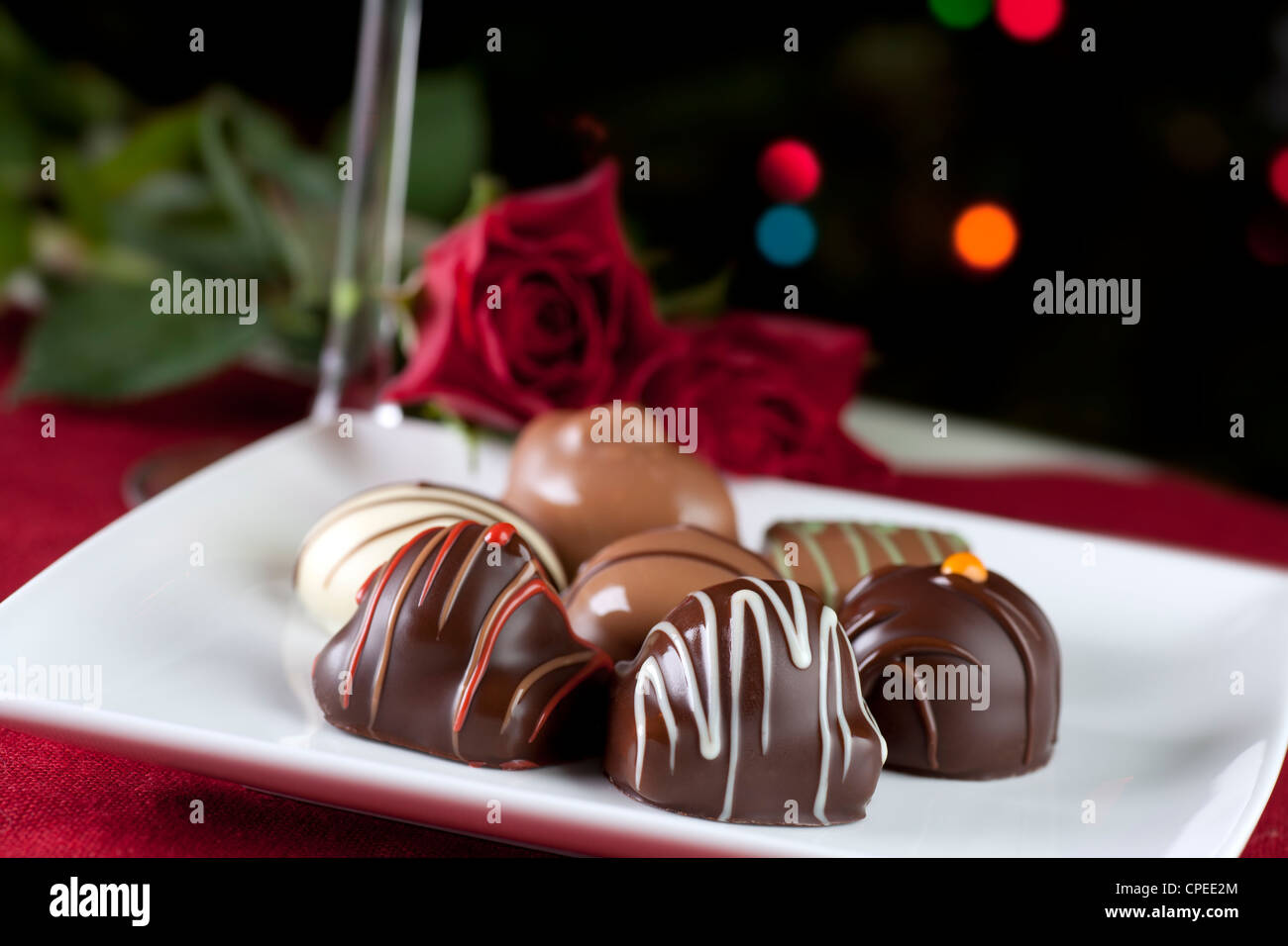 Gourmet chocolates on white plate with roses and sparkling lights. Stock Photo
