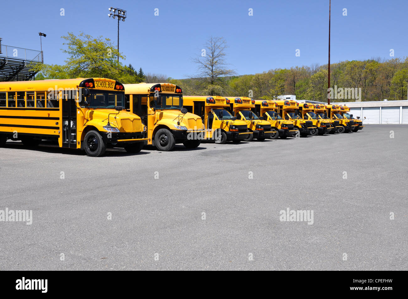row of school buses parked by a macadam parking area Stock Photo