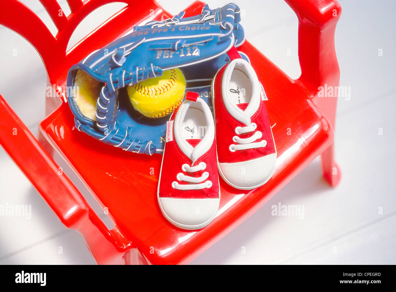 Baby Shoes, Baseball And Baseball Glove On Red Chair Stock Photo