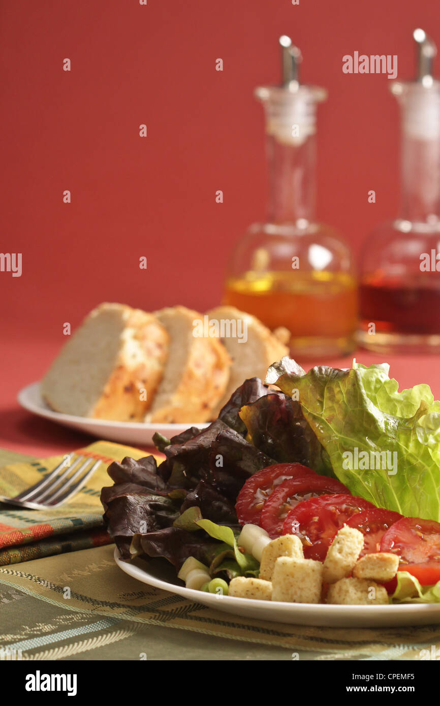 A first course dinner setting of salad, bread, and oil and vinegar on a rose colored background with a fork and a placemat. Stock Photo