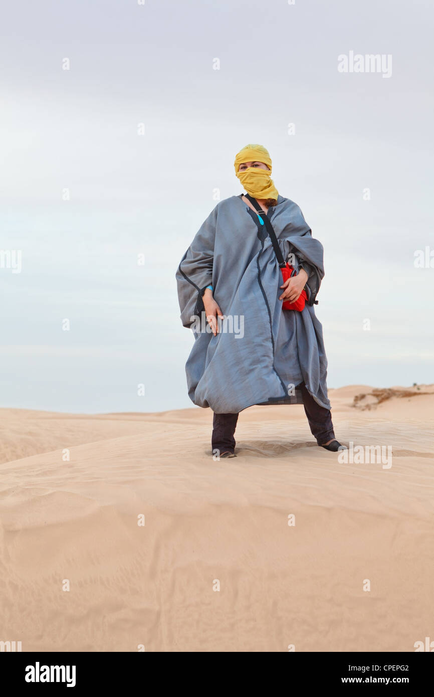 Woman in Bedouin clothes standing on dune in desert. Sahara desert, Tunisia. Vertical Stock Photo