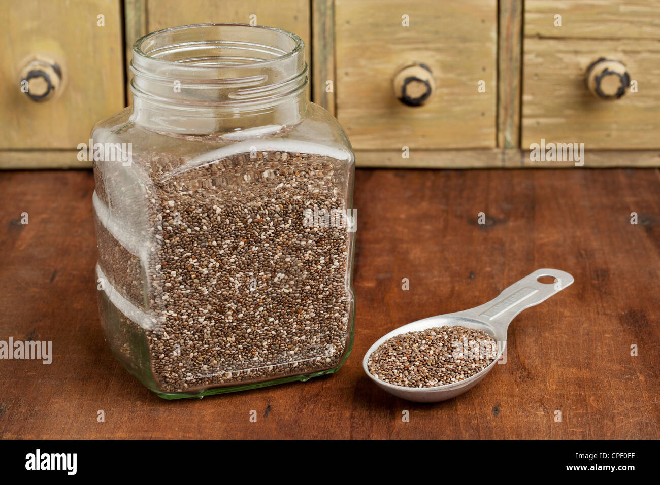 chia seeds in glass jar and on measuring aluminum tablespoon with a vintage drawer cabinet in background Stock Photo