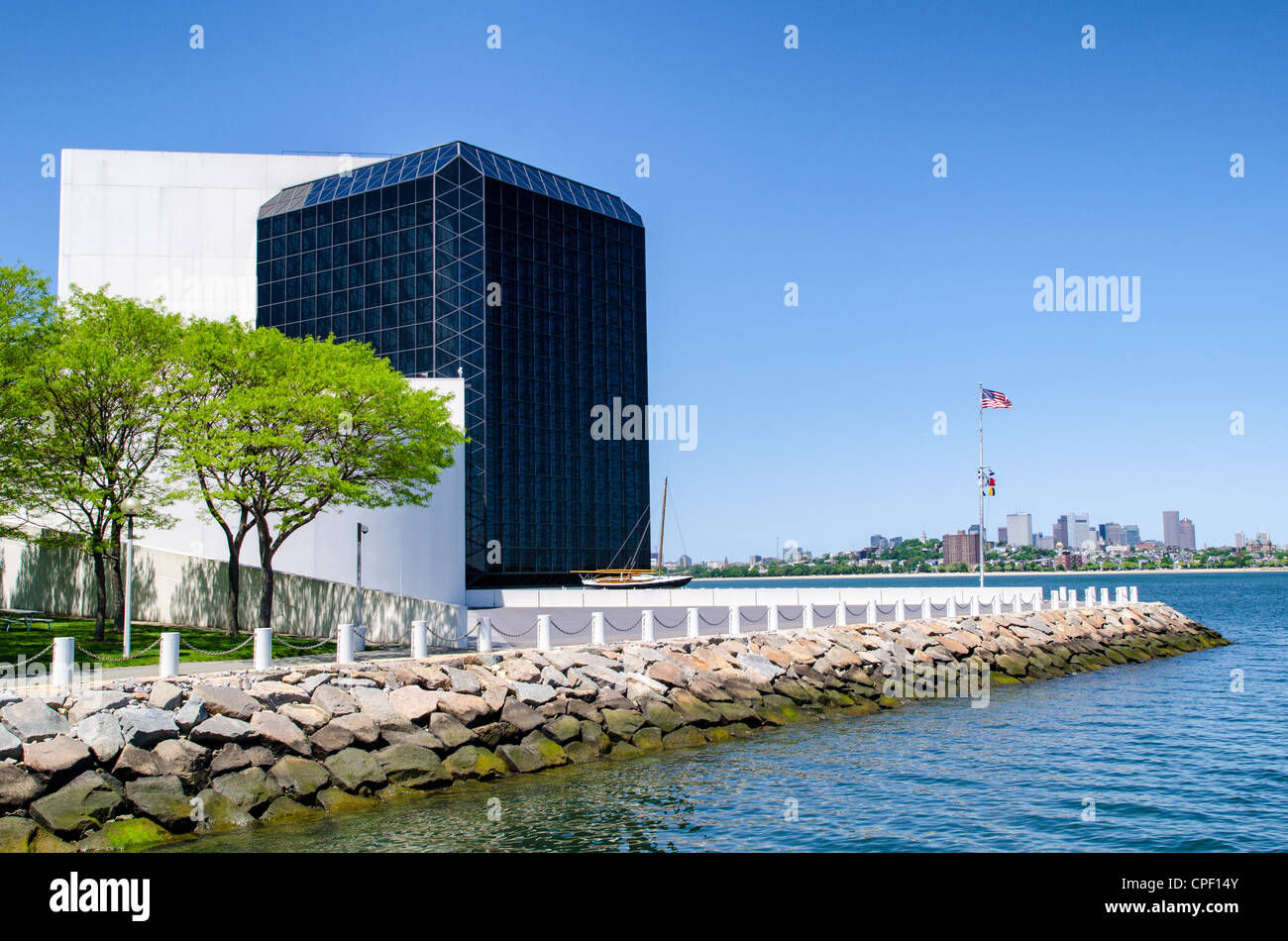 BOSTON, United States — The waterfront facade of the John F. Kennedy Presidential Library and Museum stands prominently on Columbia Point in Boston's Dorchester neighborhood, with the city's downtown high-rises visible in the distance. Designed by renowned architect I.M. Pei and dedicated in 1979, this striking modern structure houses the official National Archives and Records Administration repository for materials related to America's 35th president. The nine-story concrete and glass building features a distinctive geometric profile oriented toward Boston Harbor, symbolizing Kennedy's love o Stock Photo