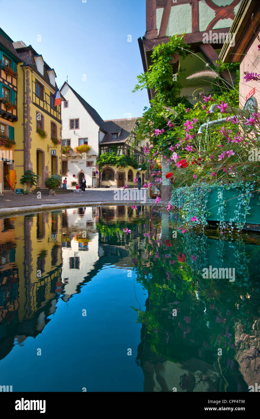Floral water fountain in central Riquewihr with Hugel wine tasting cellar in background Alsace France Stock Photo