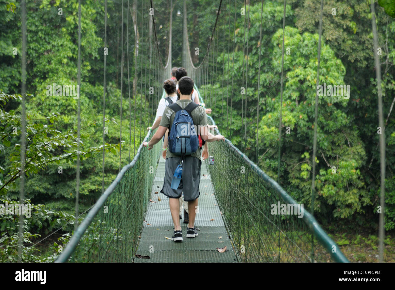 Teenagers in rainforest Costa Rica crossing a river on a suspended cable bridge Stock Photo