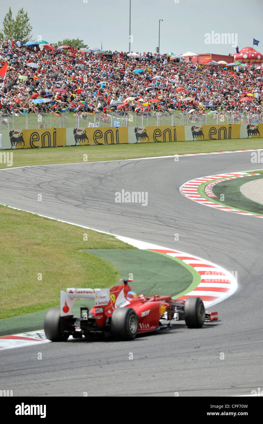 race car passes through curve in front of grandstand filled with ...