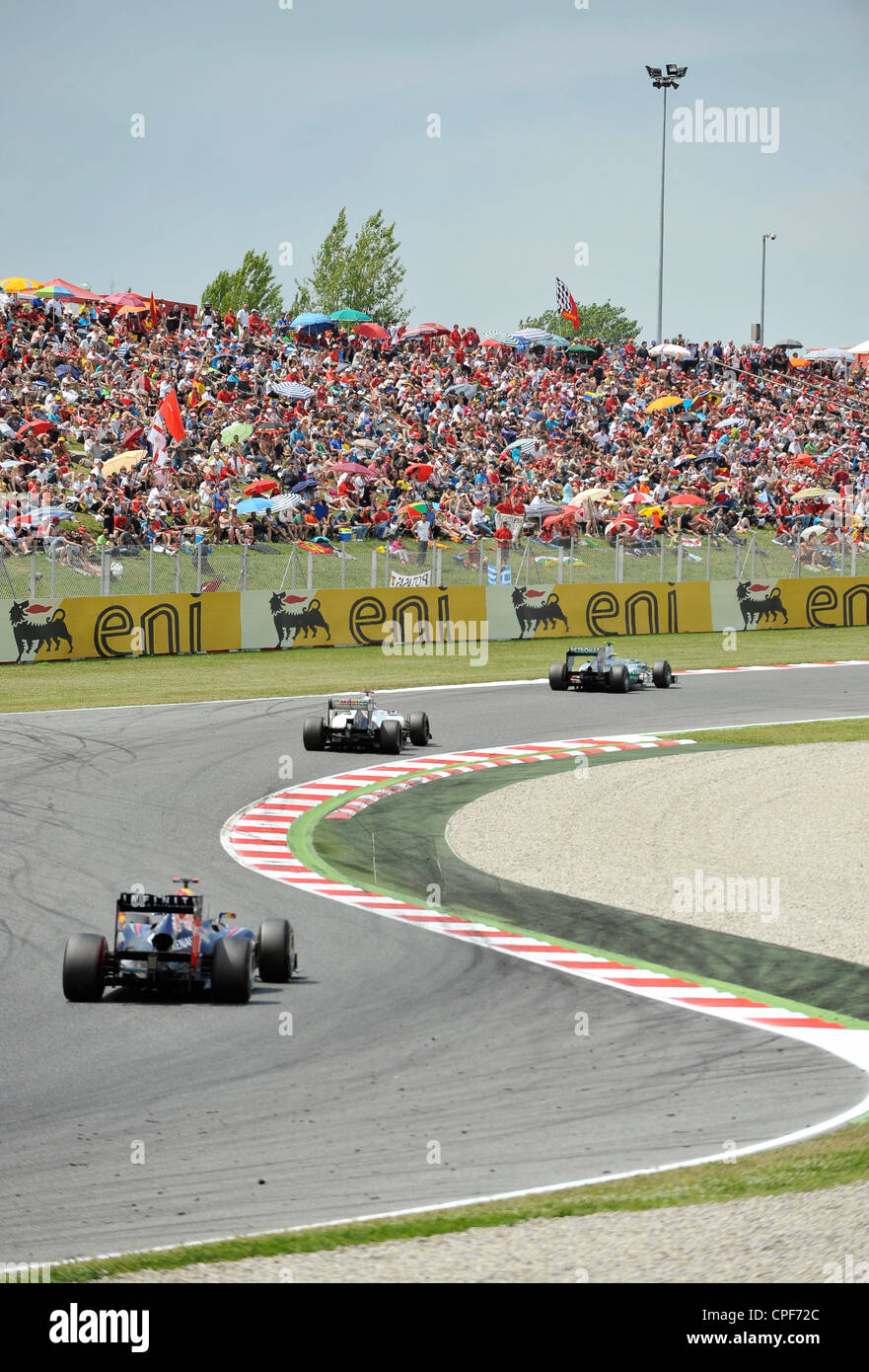 Three race cars pass through curve in front of grandstand filled with ...