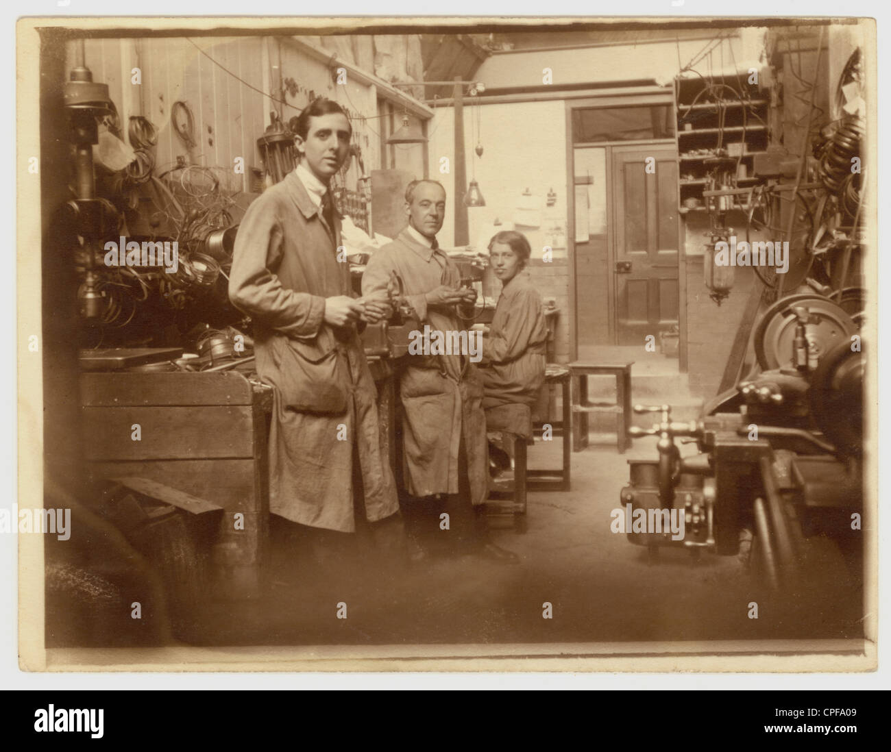 Original photo of men and a woman working in an engineering workshop, group groups occupational portrait portraits. possibly making repairs, early 1900's, Victorian, Edwardian U.K. Stock Photo