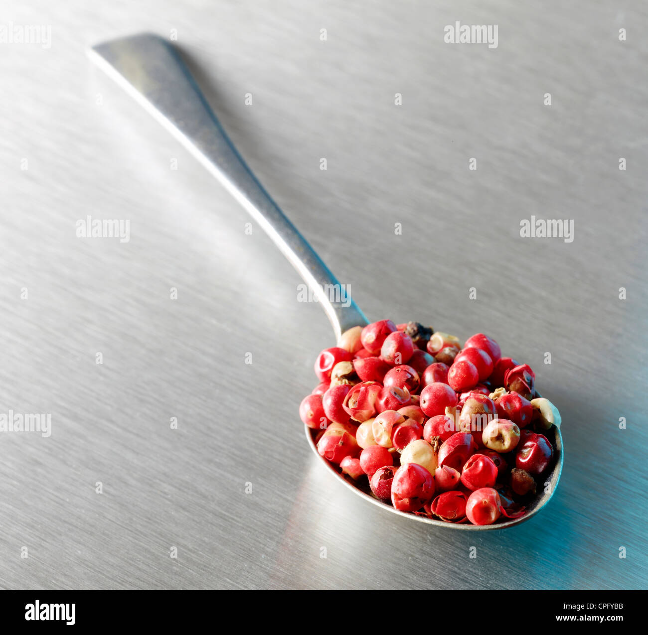 Pink peppercorns in a metal spoon on stainless steel surface Stock Photo