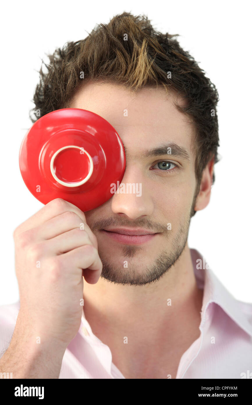 Young man holding a saucer in front of his eye Stock Photo