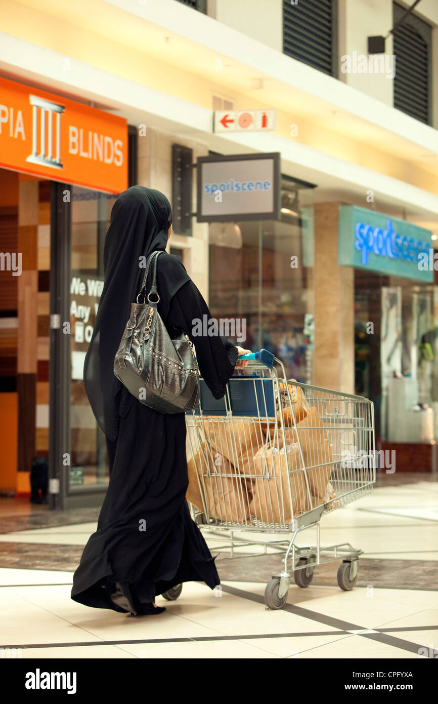 Rear view of arab woman with shopping cart walking at the mall. Stock Photo