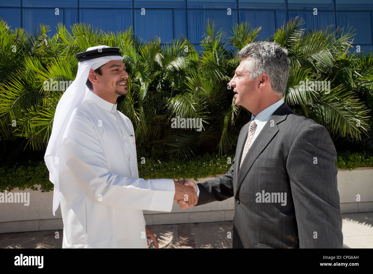 Arab businessman and western businessman shaking hands in front of office building. Stock Photo