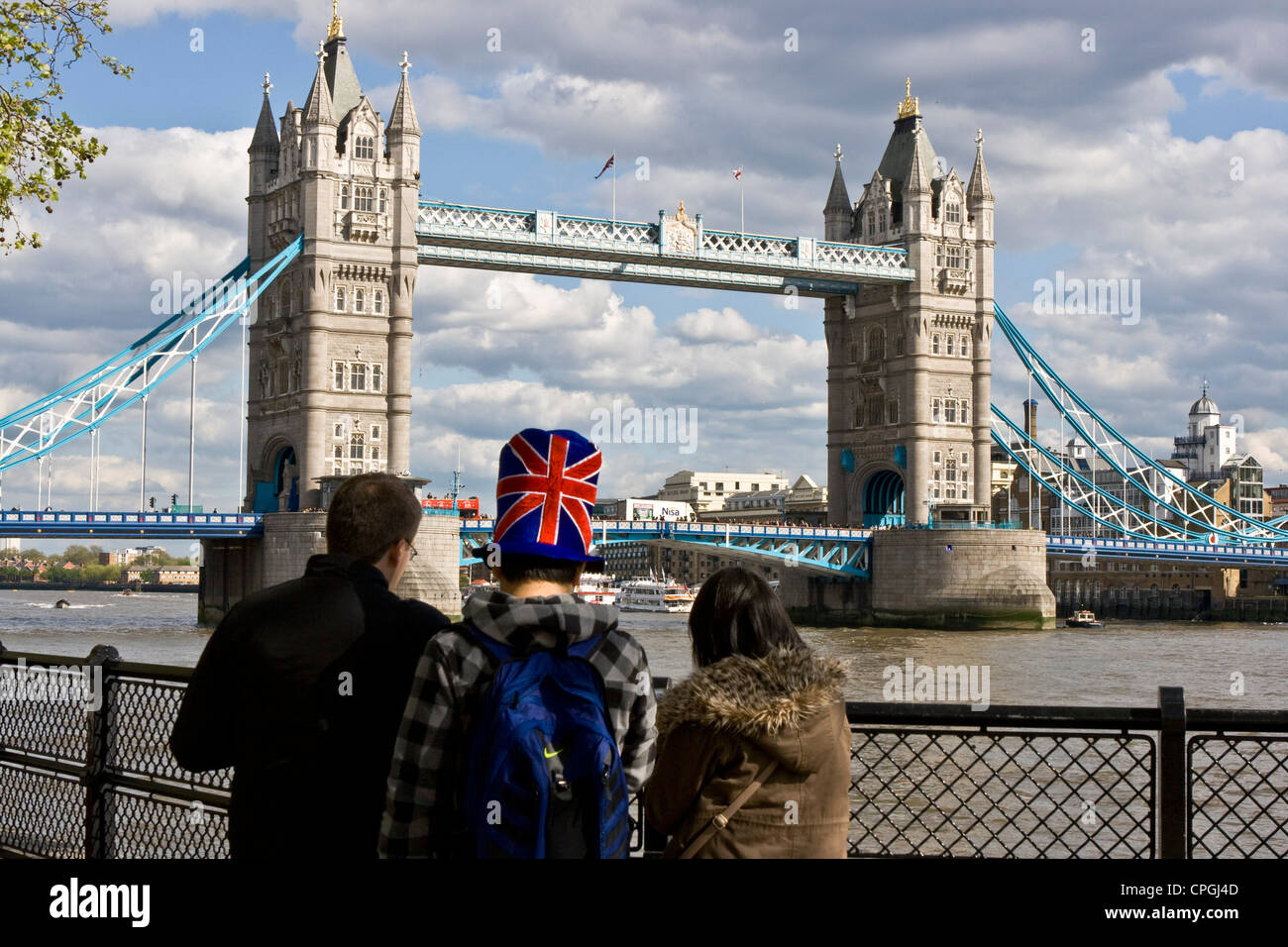 Boy holidaymaker wearing Union Jack top hat patriotic headgear looking at grade 1 listed Tower Bridge London England Europe Stock Photo