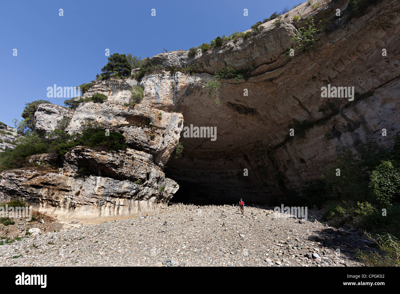Woman standing in the dry river bed at the entrance to the cave below Minerve, Llanguedoc, Herault, France Stock Photo