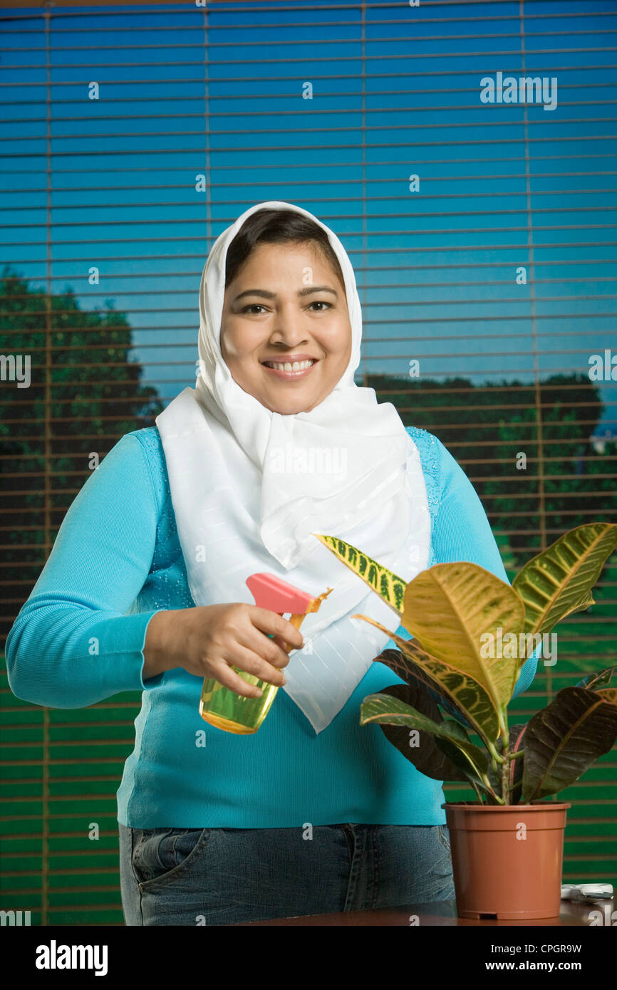 Mid adult woman spraying water to potted plant, smiling, portrait Stock