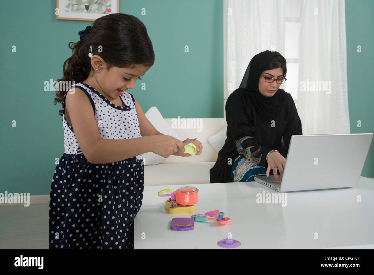 Arab mother working at home, daughter playing Stock Photo
