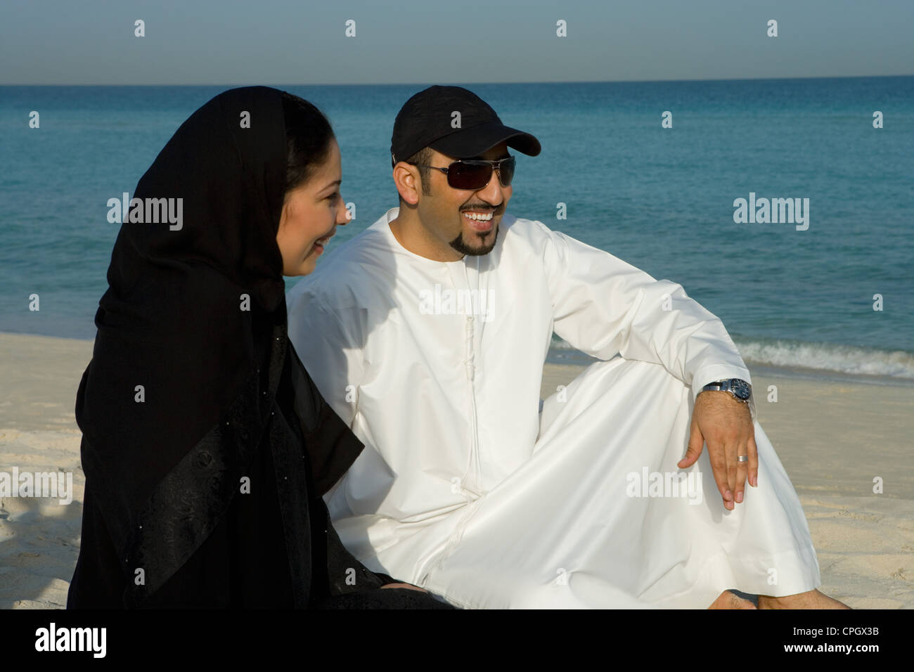 Young couple sitting on beach, smiling Stock Photo - Alamy