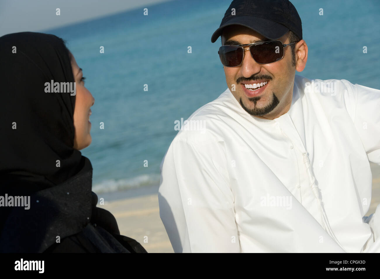 Young couple sitting on beach, smiling Stock Photo - Alamy