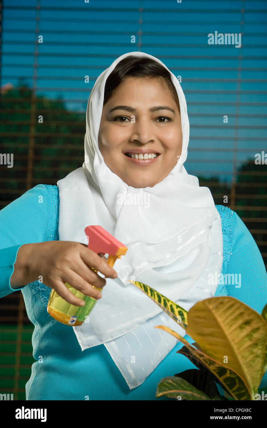 Mid adult woman spraying water to potted plant, smiling, portrait Stock