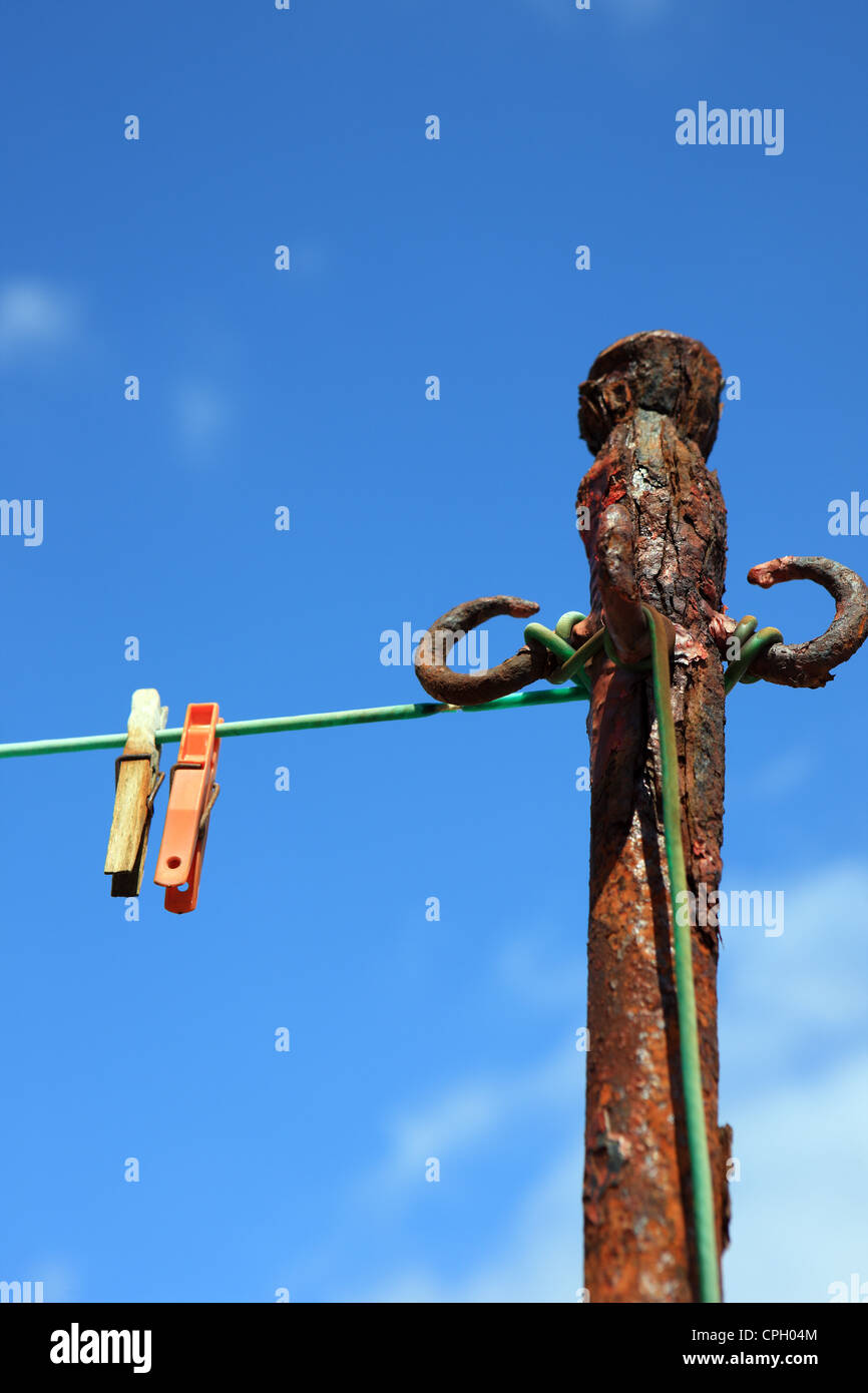 Old rusty clothes pole and two clothes pegs on a plastic rope against a blue sky Stock Photo