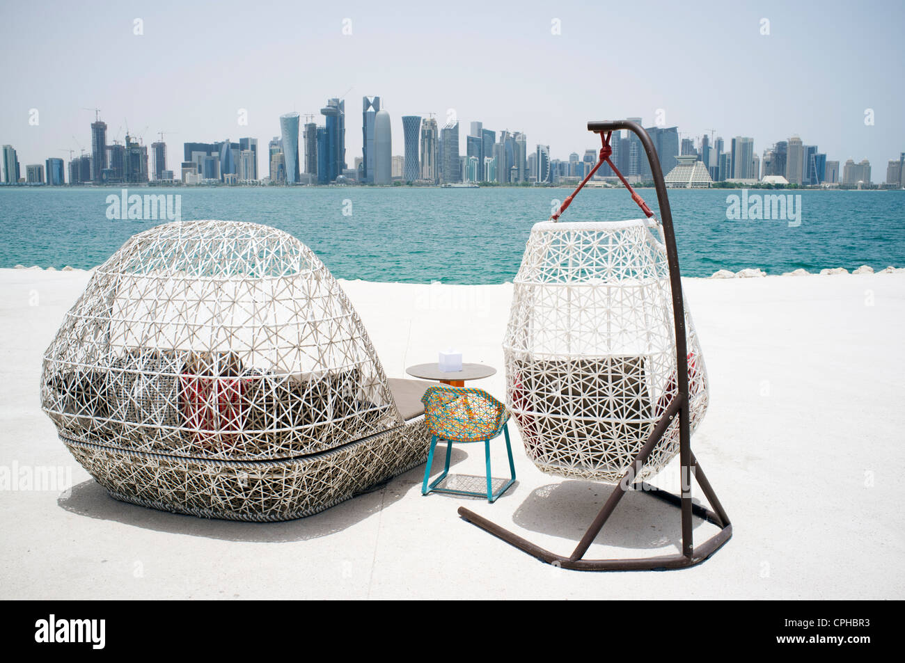 Modern outdoor seating at waterfront cafe with view of skyline of Doha ...