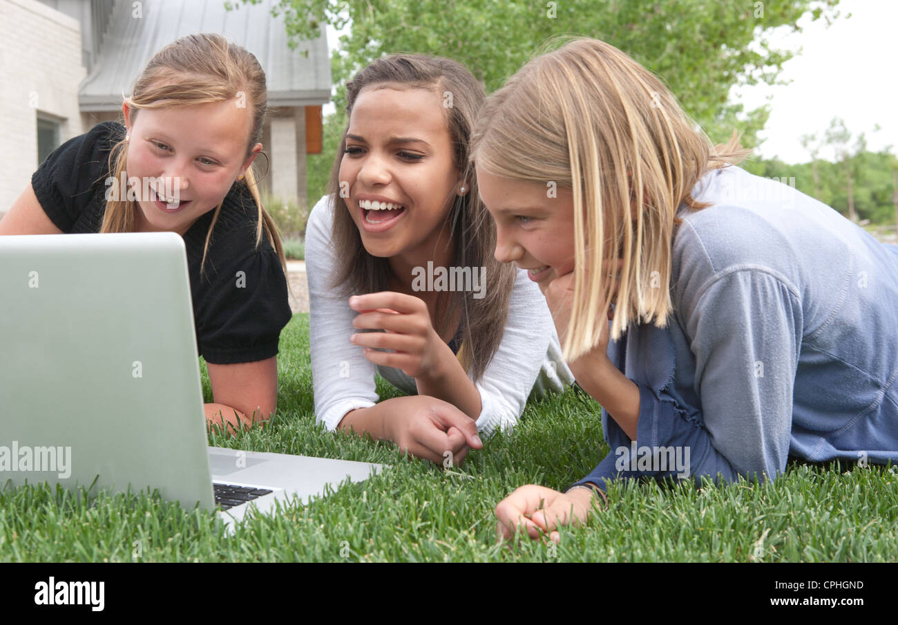 Three girls laugh at a funny internet video on a laptop outdoors. Stock Photo