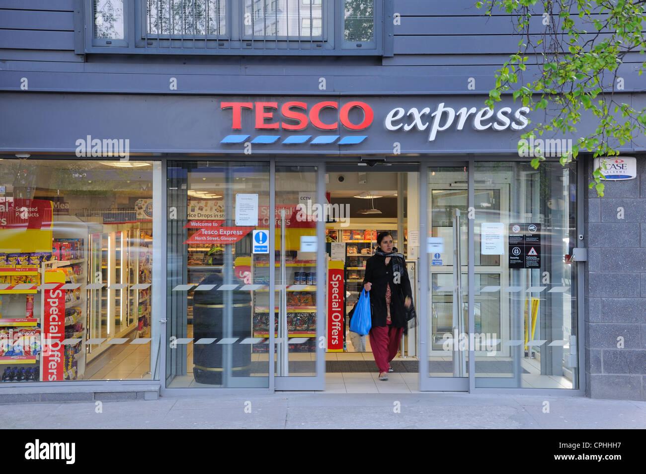 Asian woman leaves Tesco express with her shopping in Glasgow. Stock Photo