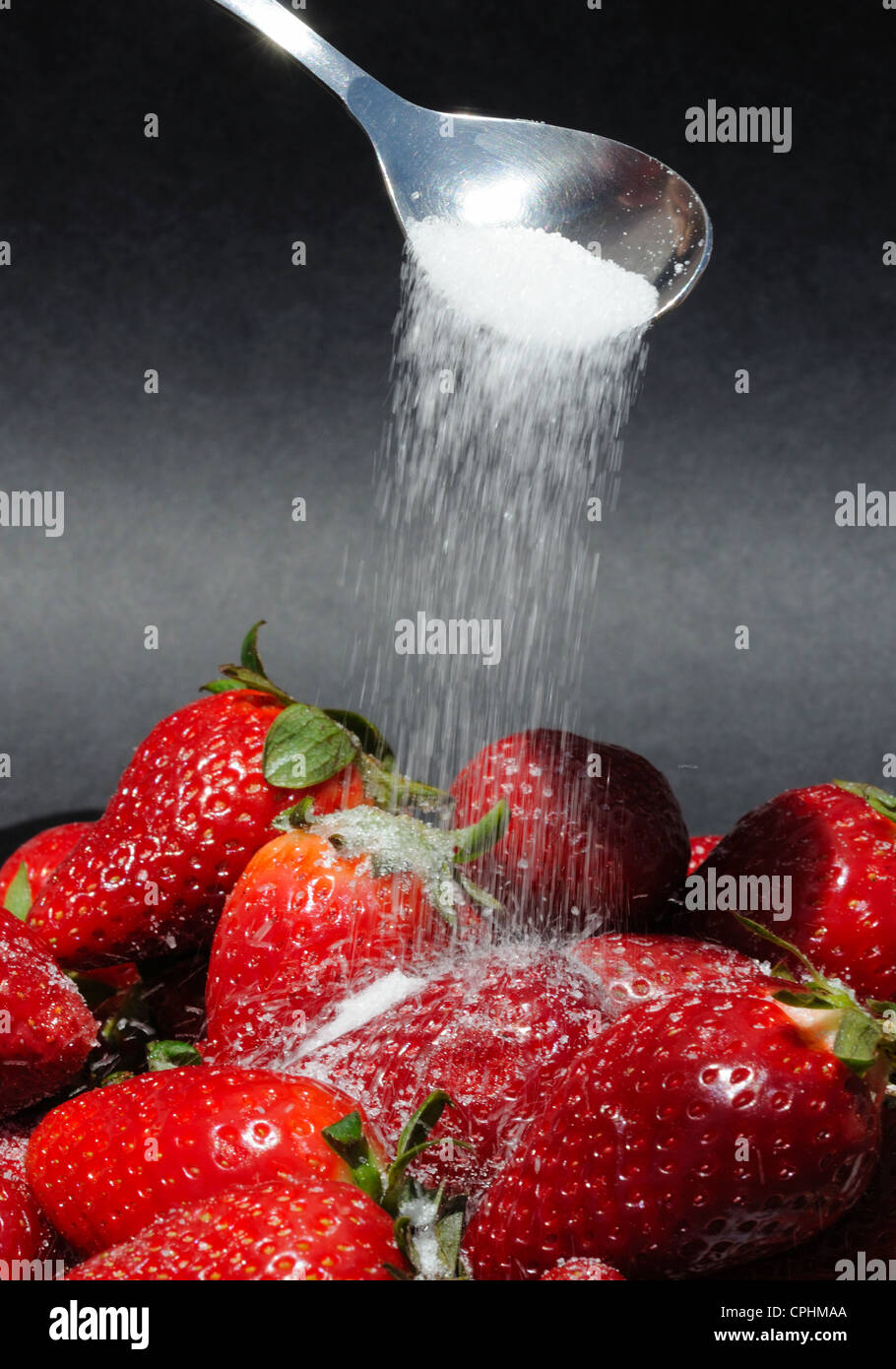 Sprinkling granulated sugar onto whole fresh strawberries. Stock Photo