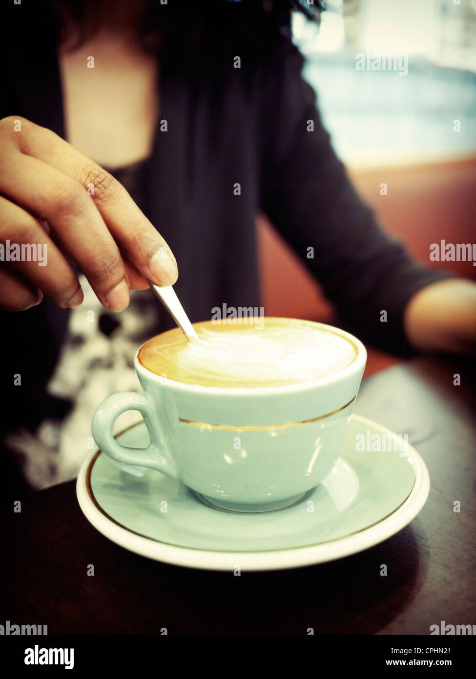 Woman stirs cup of coffee in cafe. Stock Photo