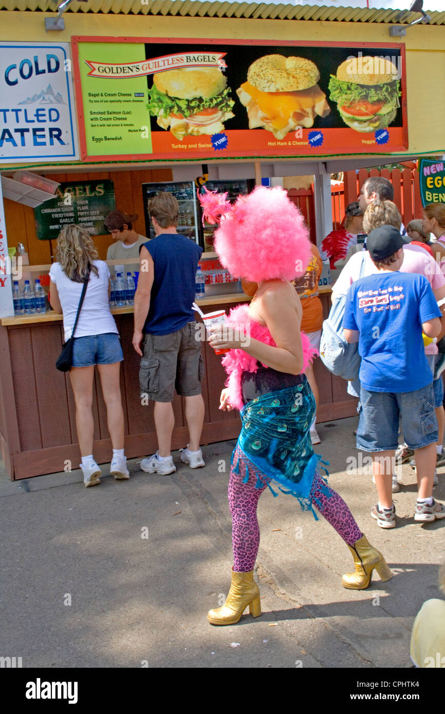 Artistically dressed woman wearing a pink wig walking by a bagel