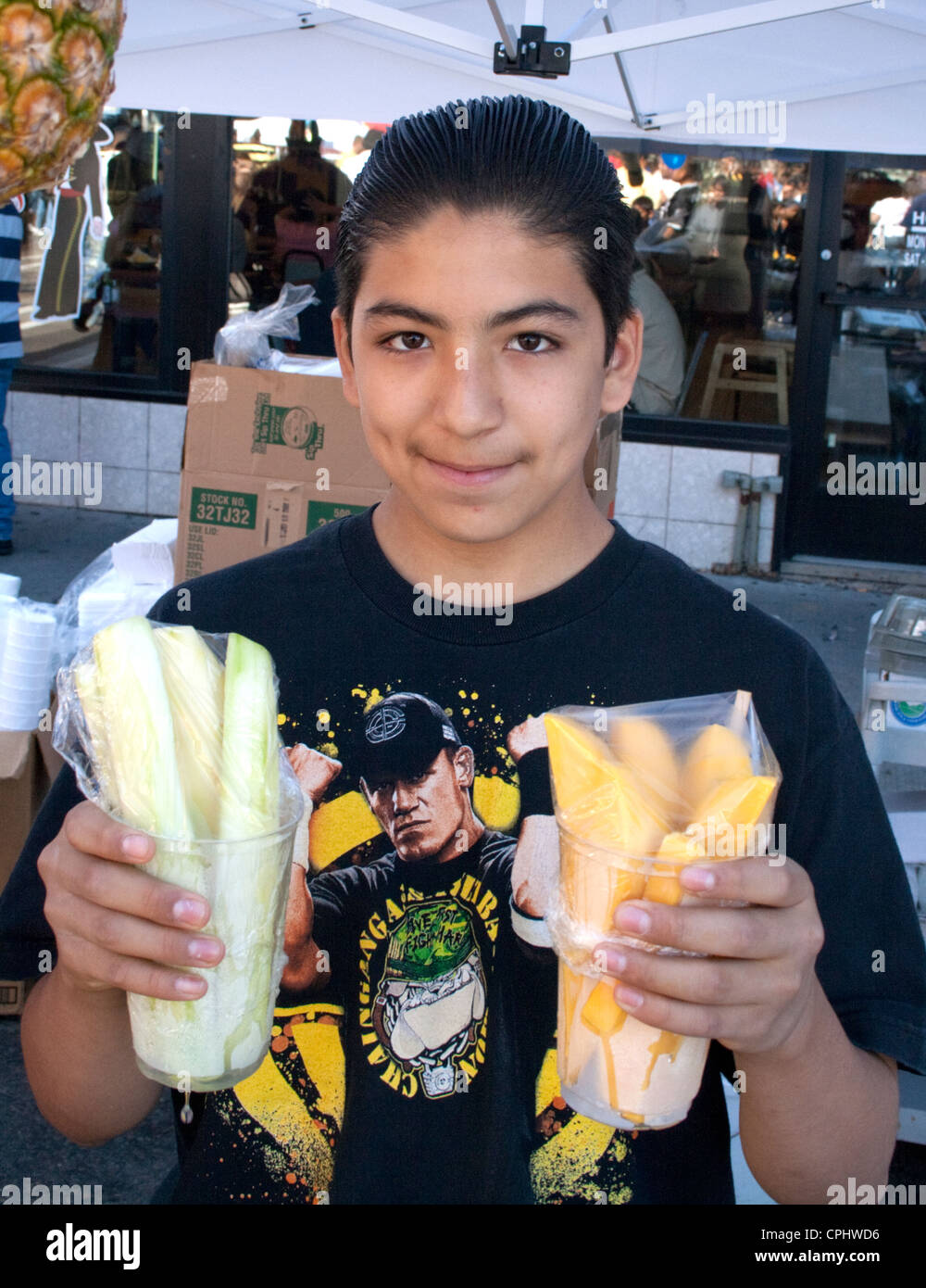 Happy Mexican American teen boy holding cups of fruit at sidewalk cafe. Mexican Independence Day Minneapolis Minnesota MN USA Stock Photo